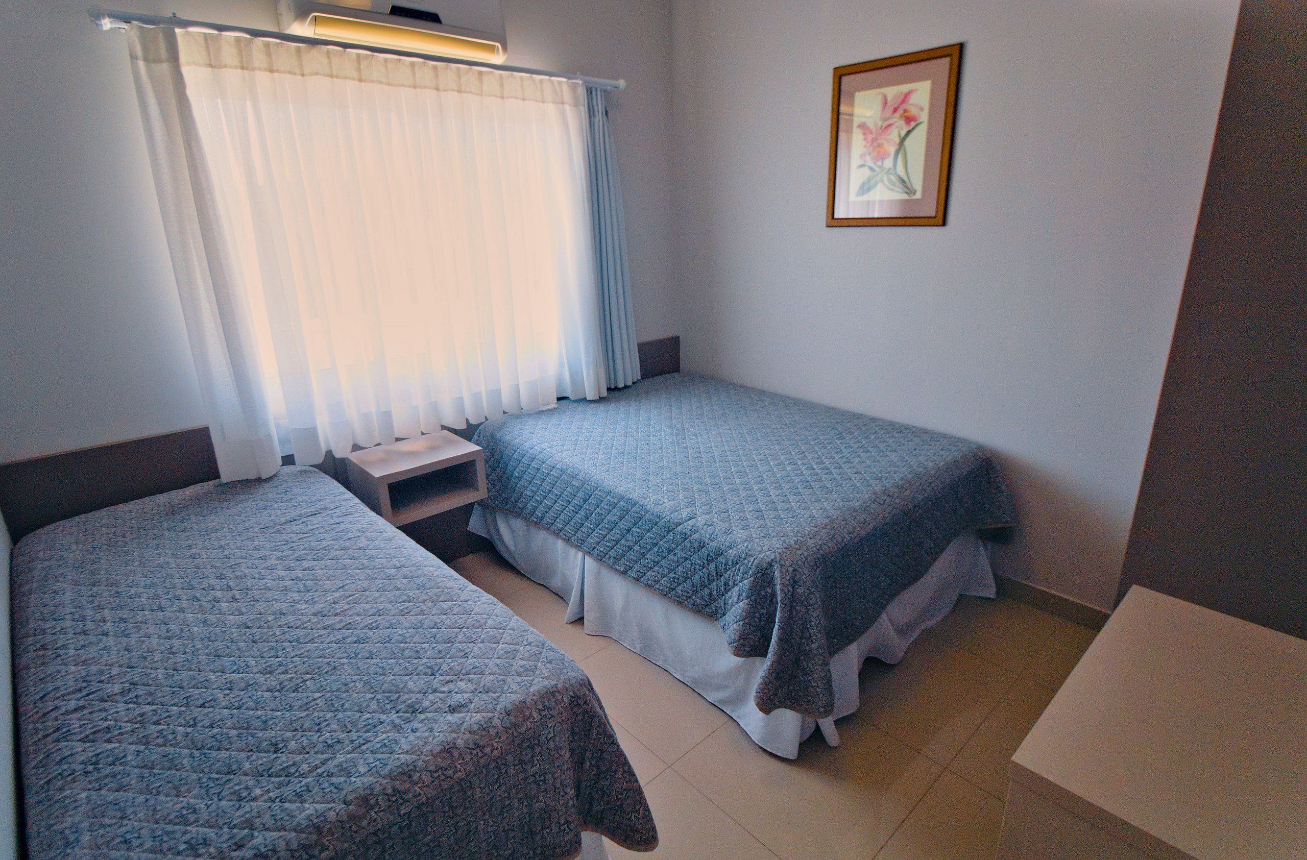A bedroom with two beds, a nightstand, and a framed picture on the wall.