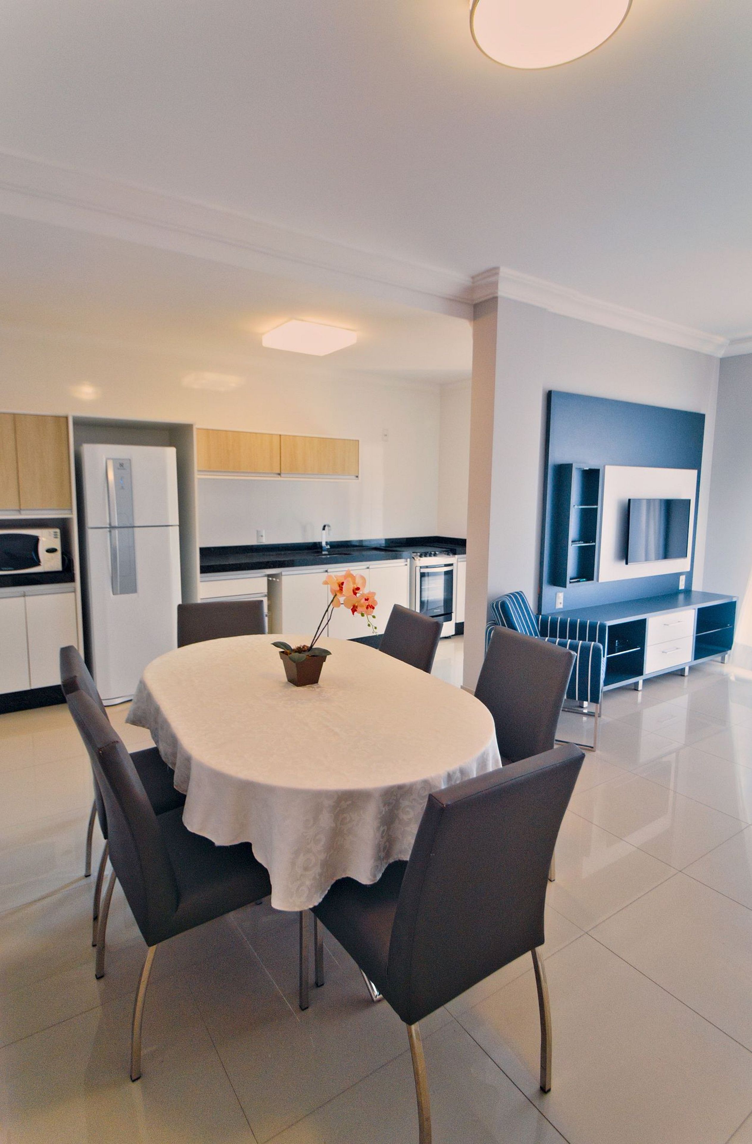 A modern kitchen with stainless steel appliances, a dining area with a round table and chairs, and a flat-screen TV mounted on the wall.