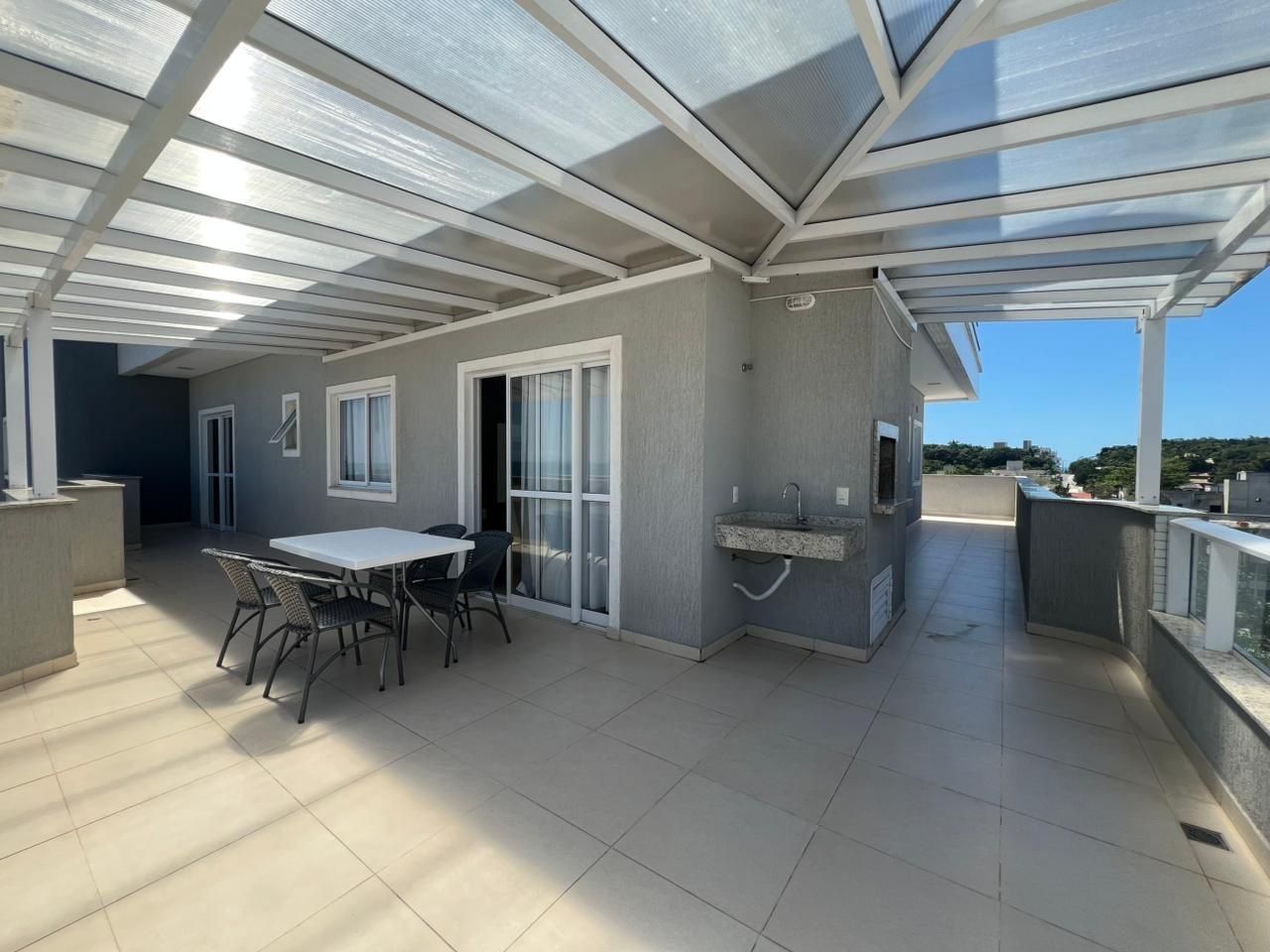 Um pátio externo com mesa, cadeiras, churrasqueira e área envidraçada.