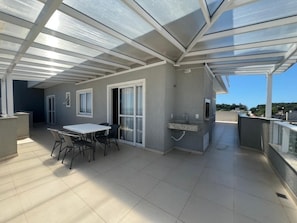 Un patio al aire libre con mesa y sillas, una parrilla incorporada y una zona cerrada con vidrio.