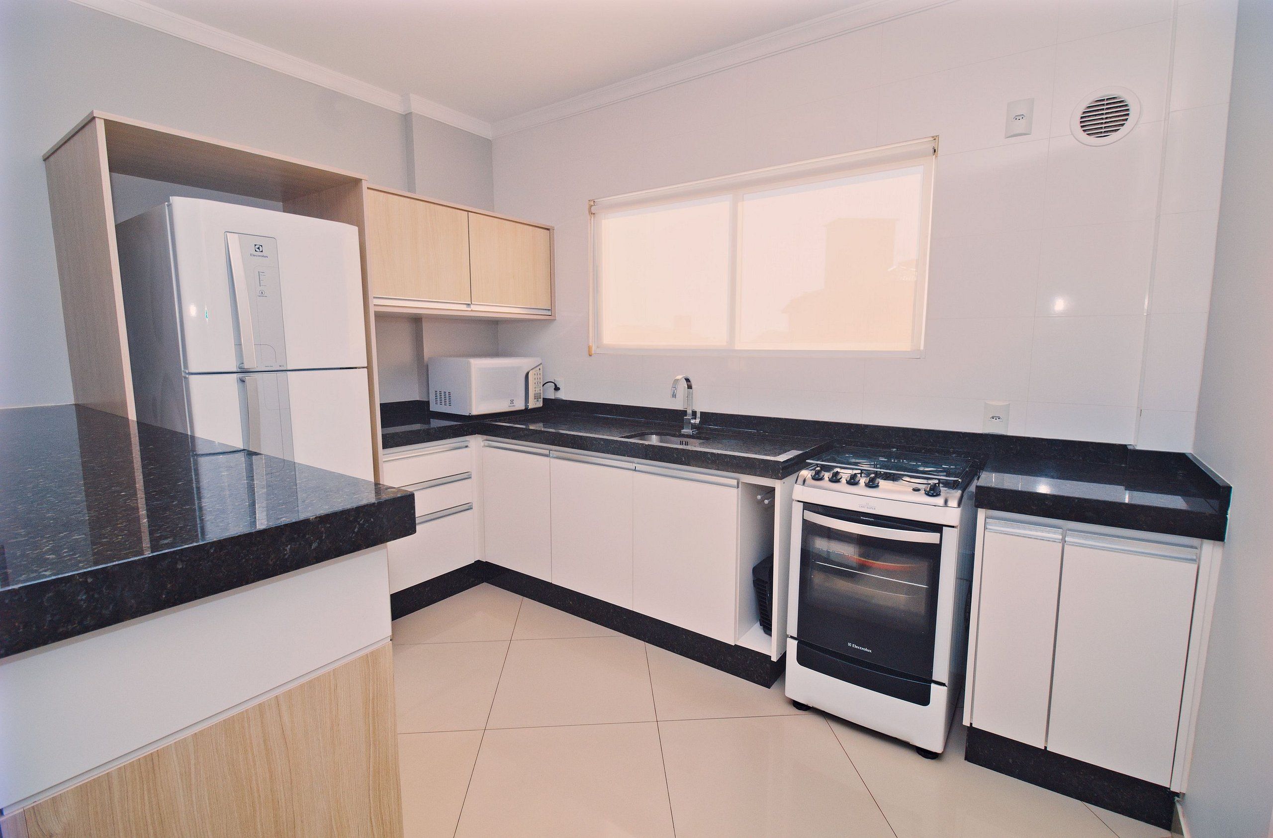 A modern kitchen with white cabinets, a black countertop, a built-in microwave, a stove, and a refrigerator.