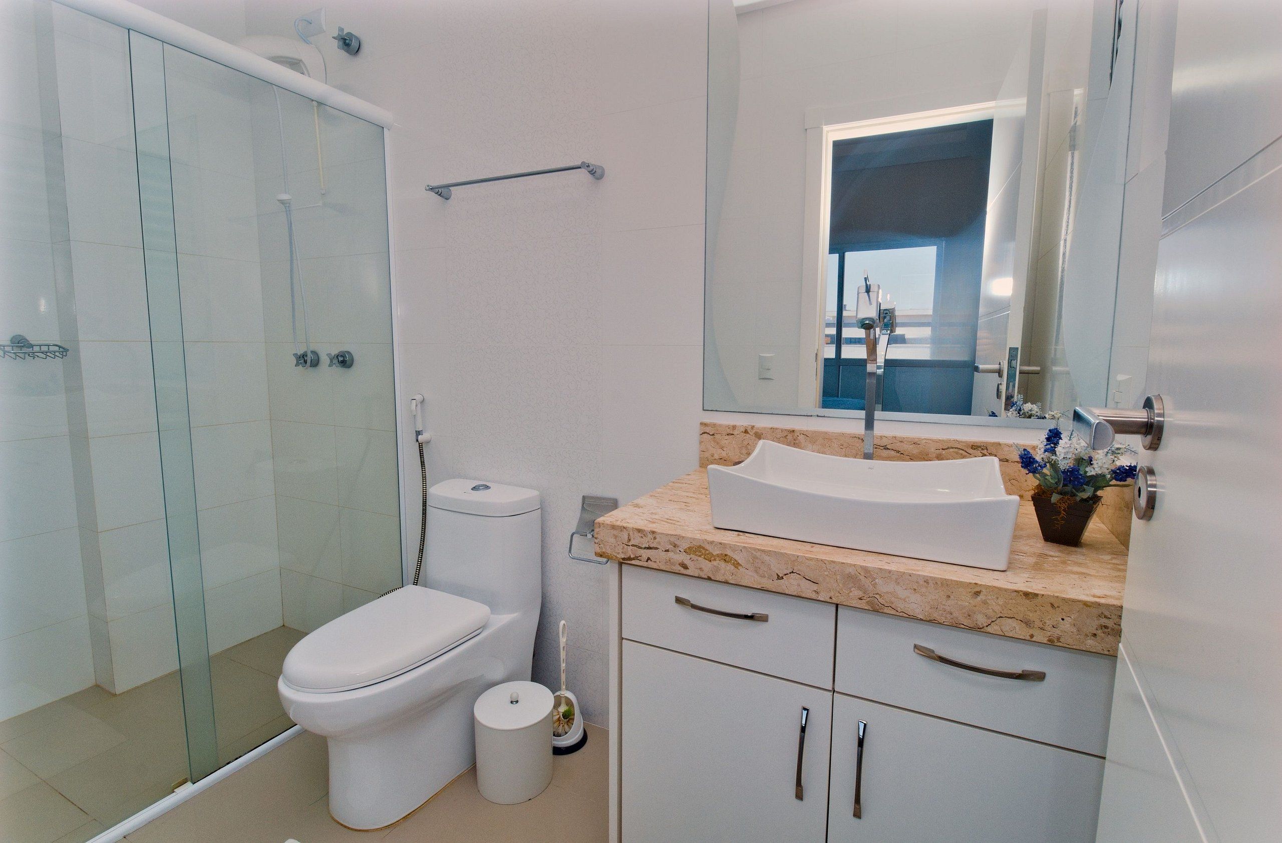 Ein modernes Badezimmer mit einer Duschkabine aus Glas, einer weißen Toilette, einem Waschbecken mit Marmorplatte und einem Spiegel über dem Waschbecken.