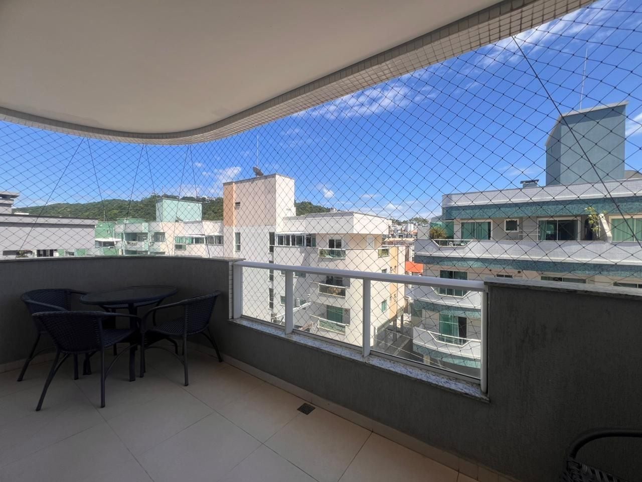 Varanda com mesa e cadeiras, vista de edifícios próximos e céu limpo.