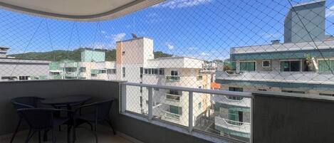 Varanda com mesa e cadeiras, vista de edifícios próximos e céu limpo.