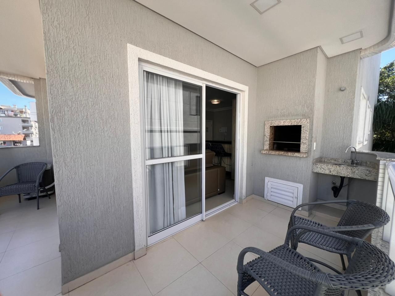 A balcony with a sliding glass door, a small sink, and wicker chairs.