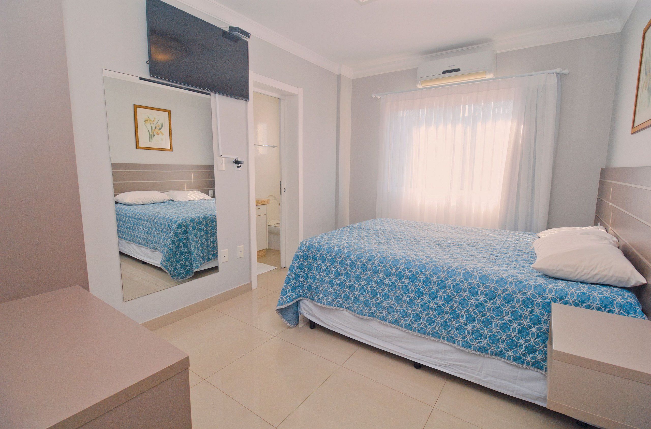 Un dormitorio con cama, espejo, mesita de noche y puerta que da a un baño.