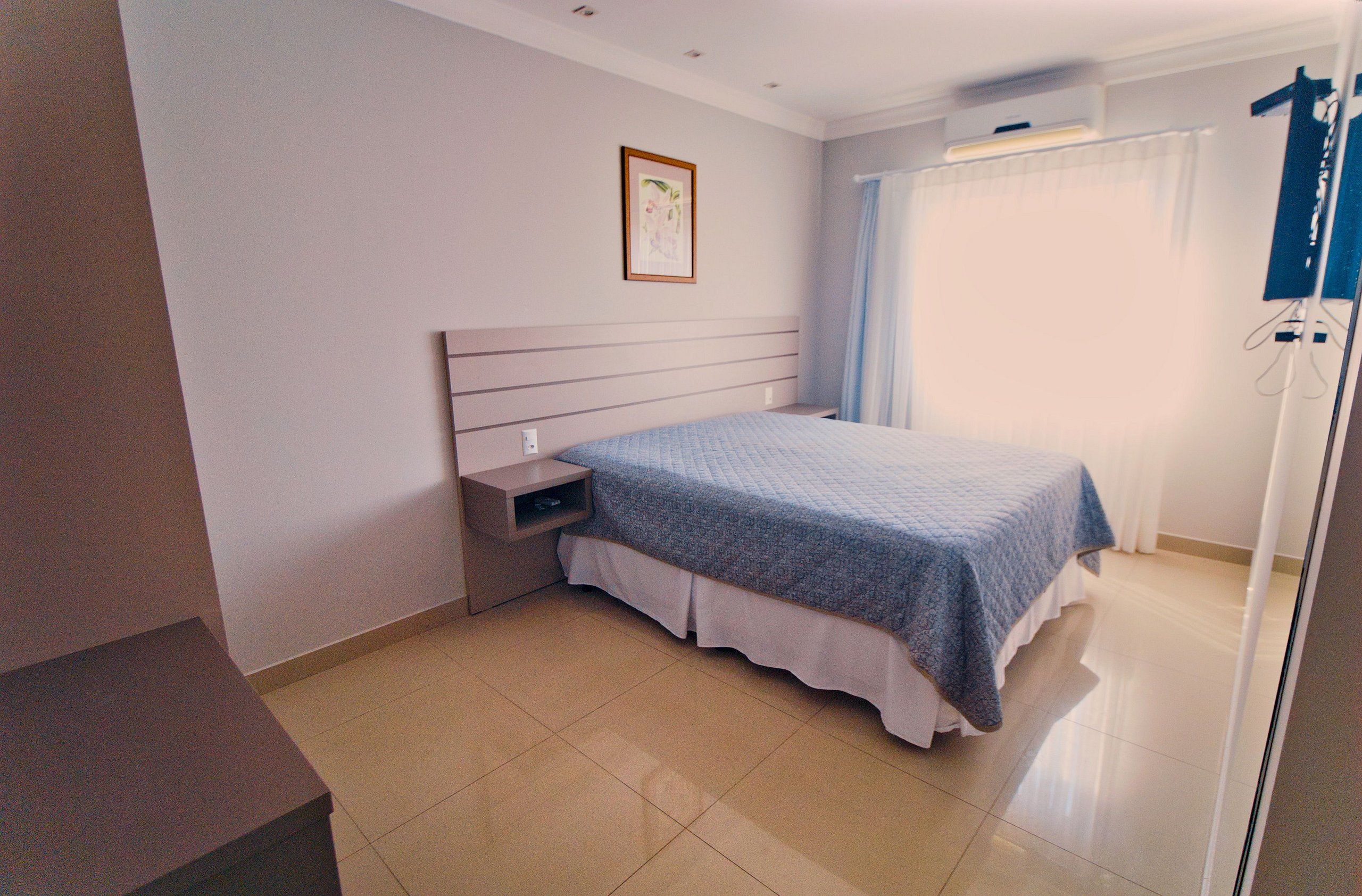 A bedroom with a bed, a nightstand, a wall-mounted air conditioner, and a window with curtains.