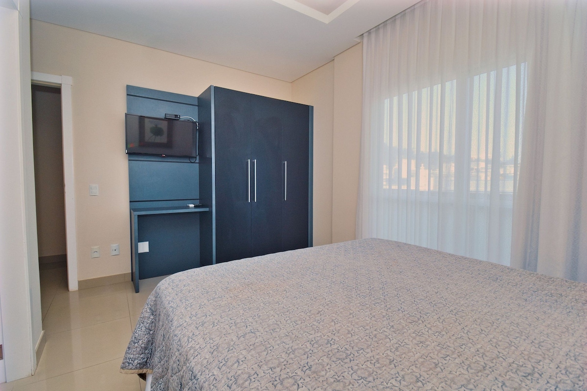 A bedroom with a bed, a wardrobe, a desk, and a television.
