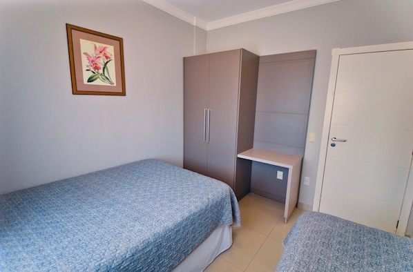 Un dormitorio con dos camas individuales, un armario, un escritorio y una puerta.