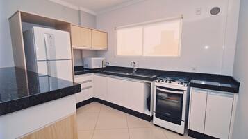 A modern kitchen with white cabinets, a black countertop, a built-in microwave, a stove, and a window above the sink.