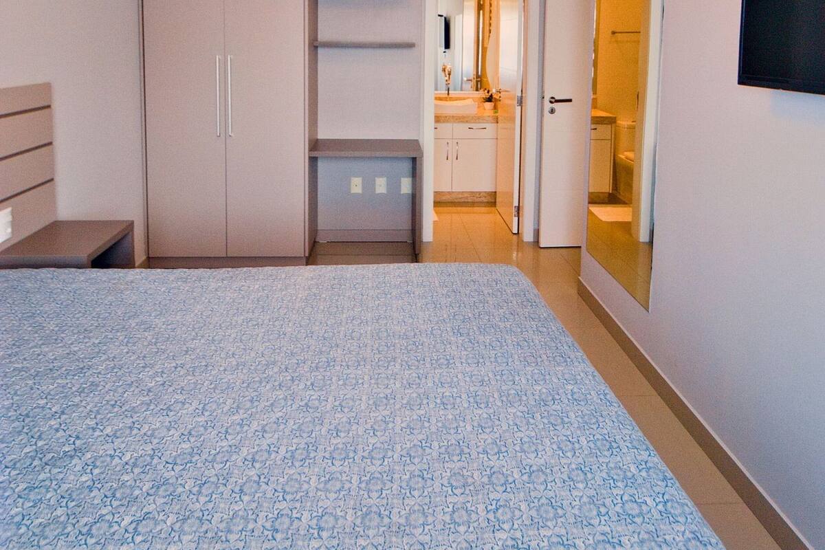 Une chambre à coucher avec un lit, une armoire, un miroir et une salle de bain visible à travers une porte ouverte.