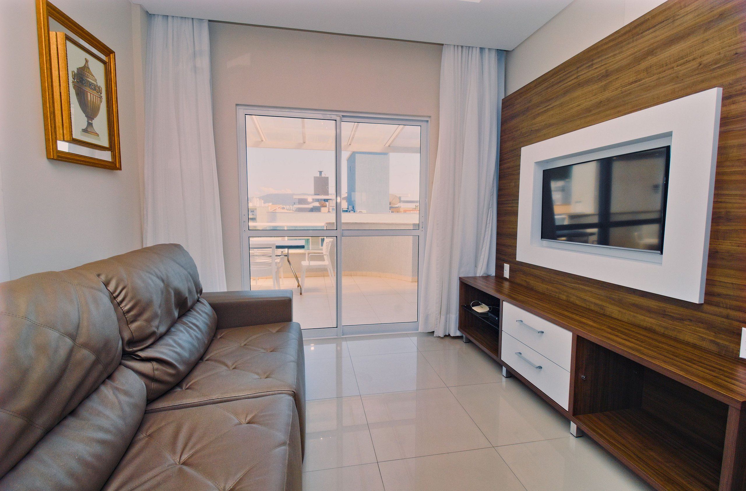 Un salon moderne avec un canapé en cuir, un téléviseur fixé sur un mur en bois et une porte-fenêtre coulissante donnant sur un balcon.