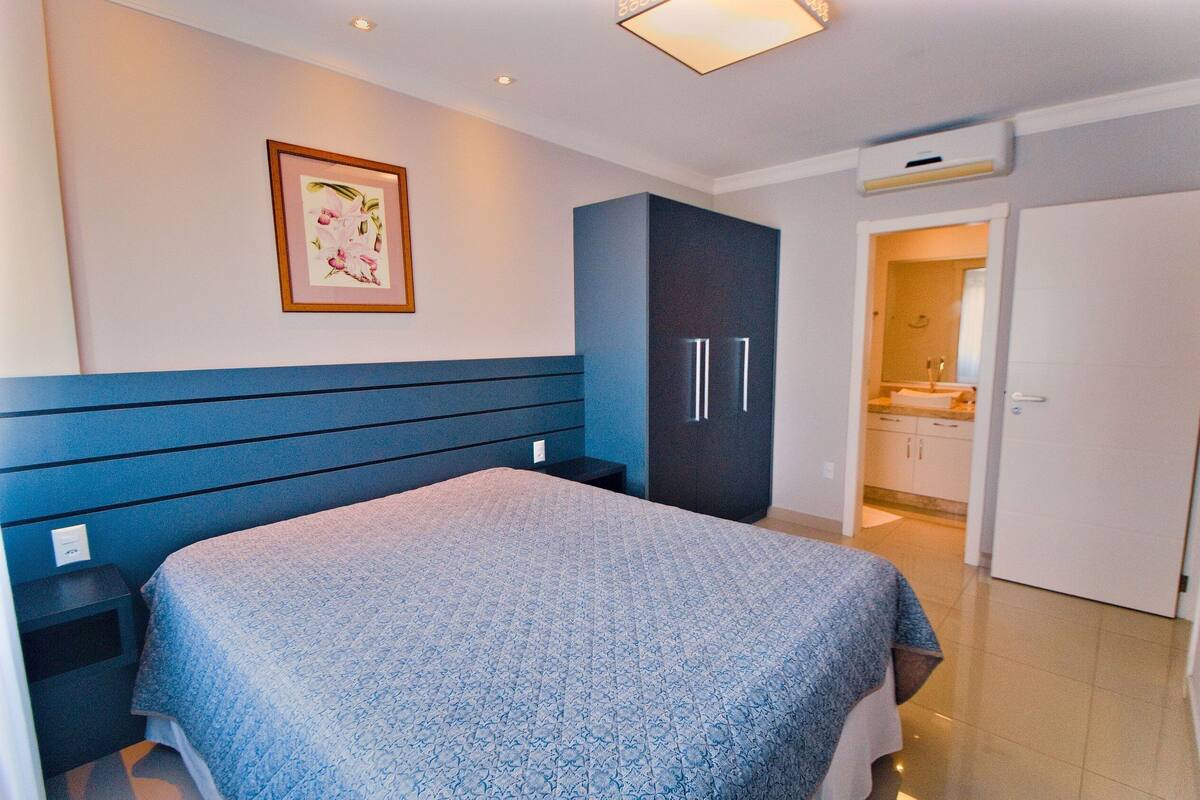 Une chambre à coucher avec un lit, une armoire et une salle de bain visible à travers une porte ouverte.