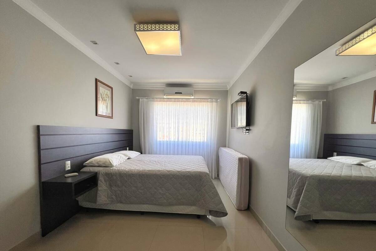 Une chambre d’hôtel moderne avec un grand lit, une table de chevet, un miroir et un luminaire au plafond.