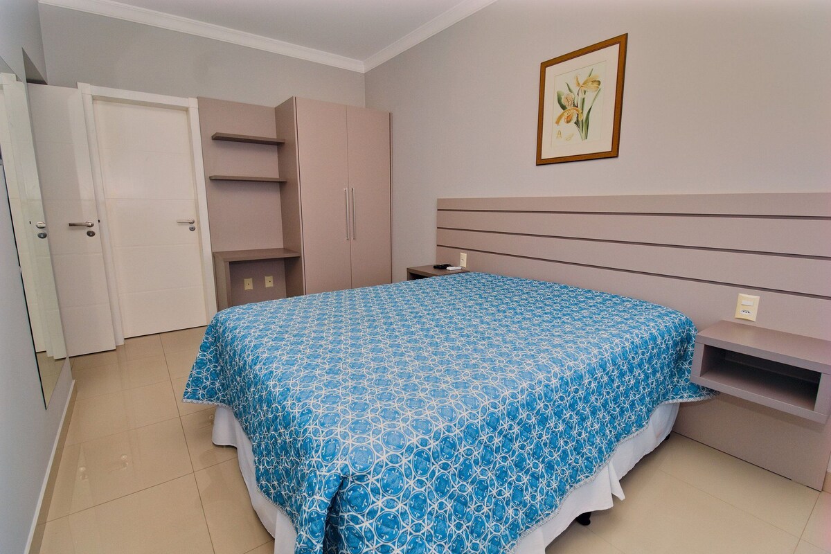 A bedroom with a bed, a wardrobe, a nightstand, and a framed picture on the wall.