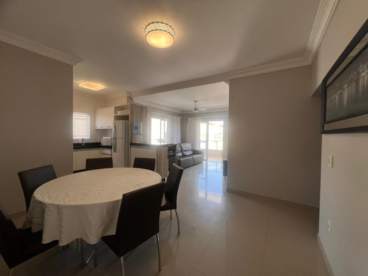 A spacious living room with a round dining table, a kitchen area, and a view of the outside.