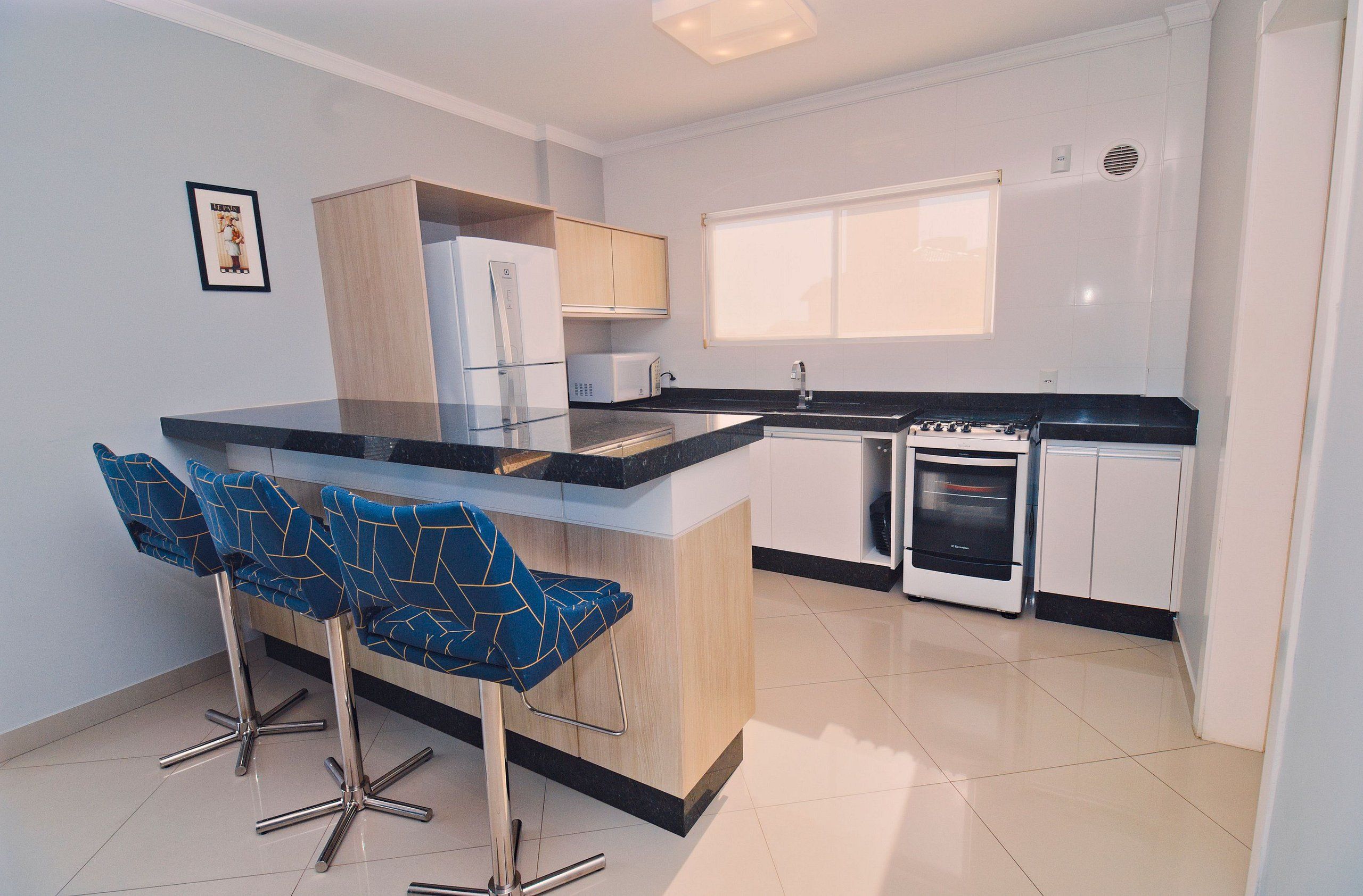 Een moderne keuken met een centraal eiland, barkrukken, een koelkast, een magnetron en een fornuis.