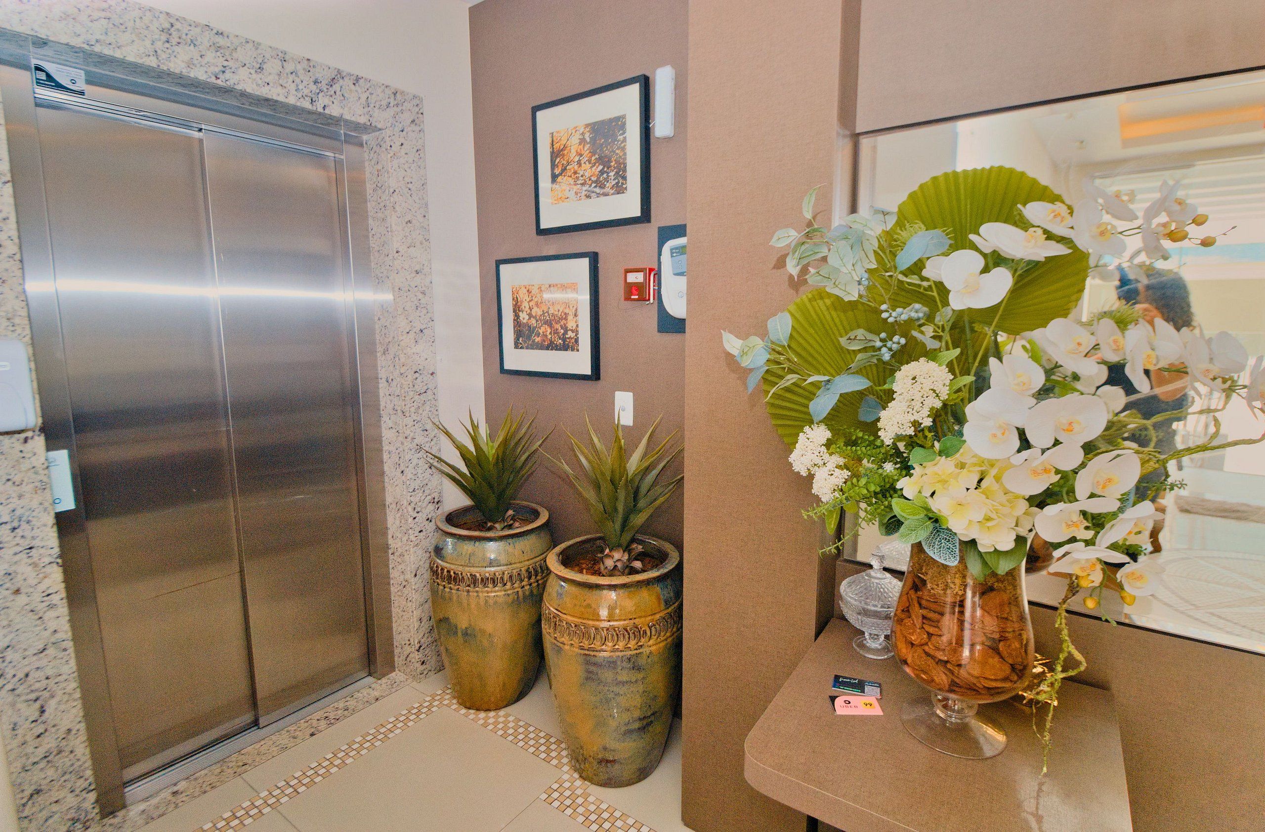 An elevator, two large potted plants, and a vase with flowers in a lobby area.