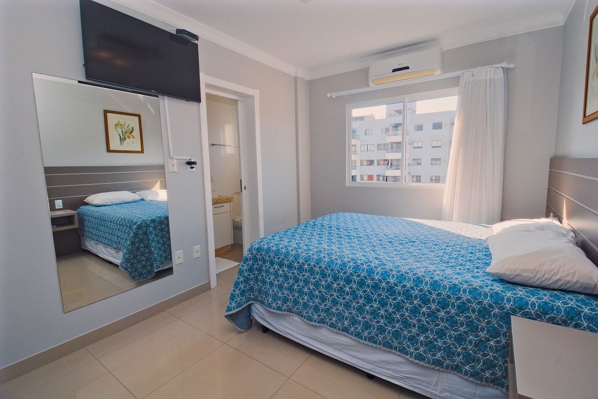 Une chambre à coucher avec un lit, un miroir, une fenêtre et une porte.