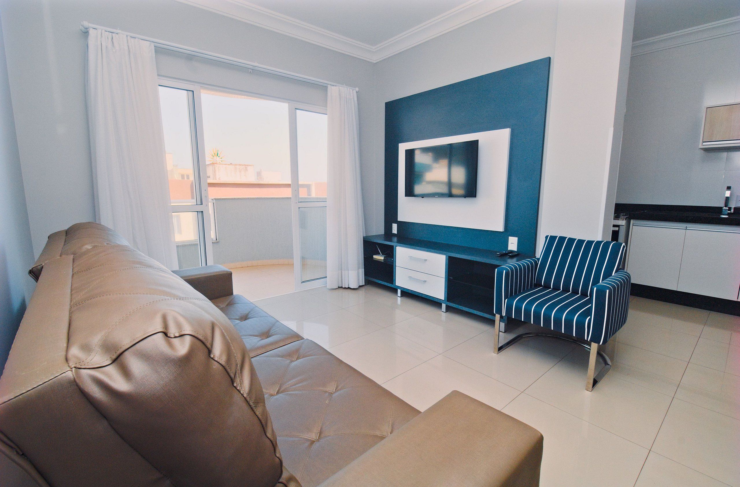 A modern living room with a sofa, a striped armchair, a flat-screen TV, and a kitchen area.