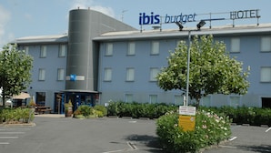 A hotel named ibis budget with a modern design, featuring a large cylindrical structure, a parking area, and a sign indicating a 30-minute parking reserve. - Ibis Budget Libourne (Libourne)