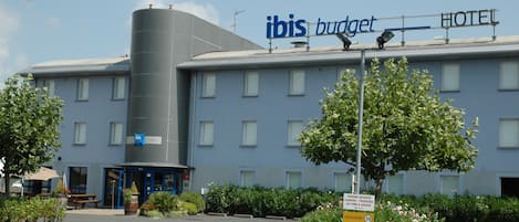 Un hotel llamado ibis budget con un diseño moderno, que presenta una gran estructura cilíndrica, un área de estacionamiento y un cartel que indica una reserva de estacionamiento por 30 minutos.