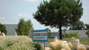 A sign for Liborne-Plage with a backdrop of a pine tree and dry grass. - Ibis Budget Libourne (Libourne)