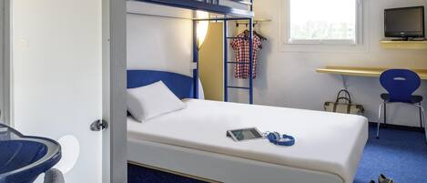A hotel room with a bunk bed, a desk with a computer, a chair, a TV, and a pair of shoes on the floor.