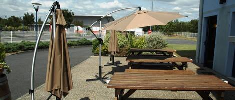 An outdoor seating area with picnic tables and umbrellas, a lamp post, and a building in the background.