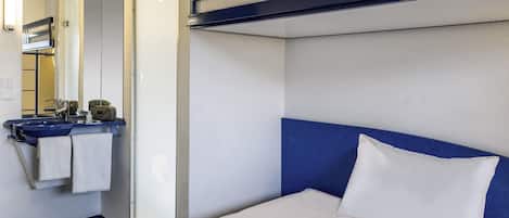 A hotel room with a bunk bed, a bedside table with a tablet and headphones, a sink with a towel, and a mirror.