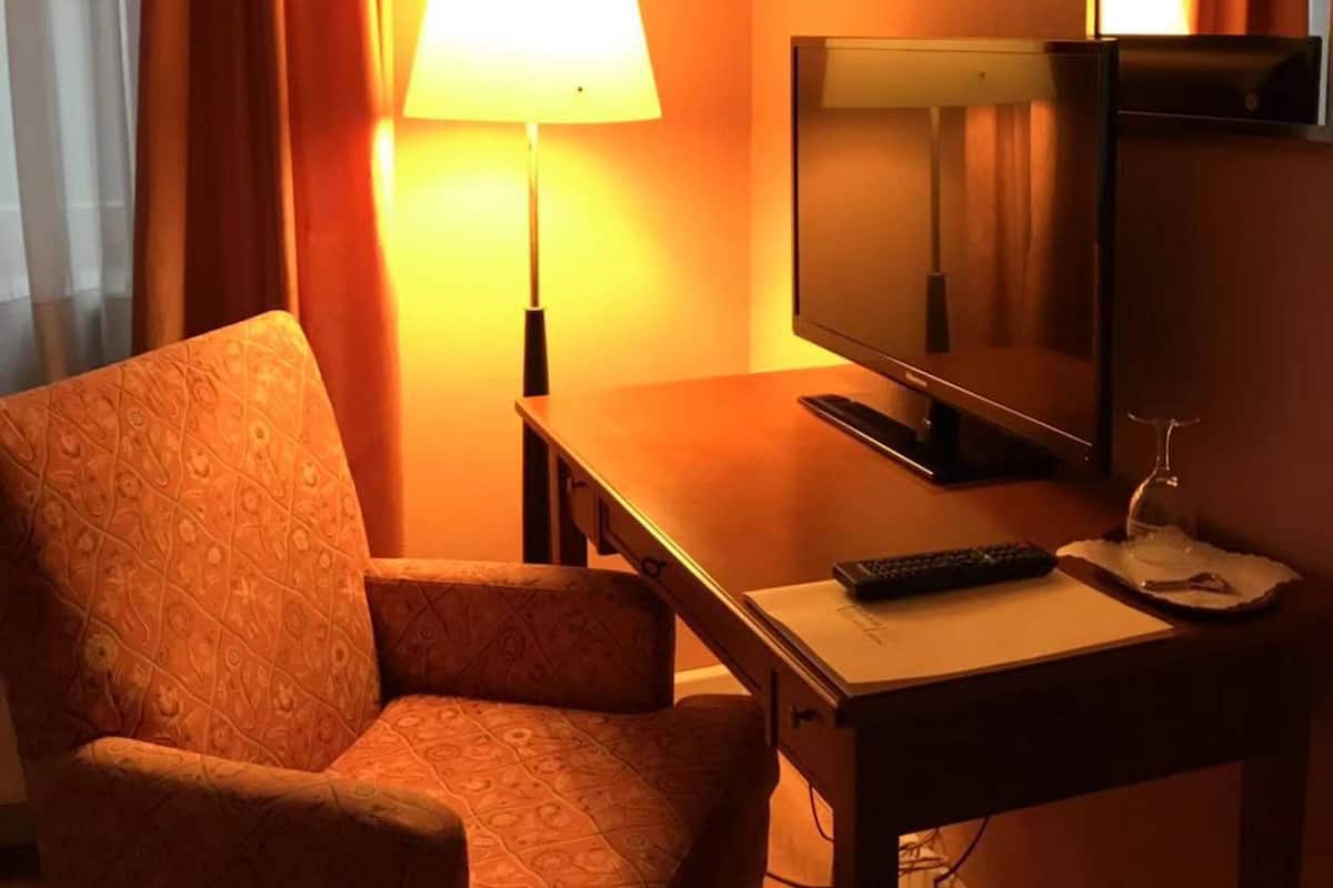 Une chambre d’hôtel avec un lit simple, un bureau avec une télévision, une lampe et une télécommande.