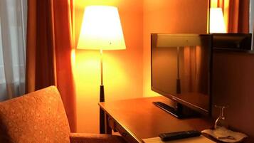 A hotel room with a single bed, a desk with a television, a lamp, and a remote control.