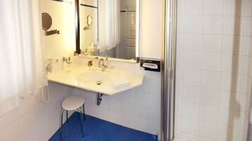 Un baño con lavamanos blanco, espejo y zona de ducha.