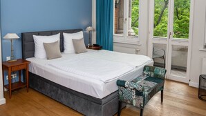 A bedroom with a bed, bedside tables, a bench, and a window with a view of greenery. - Hotel Villa Viktoria Luise (Blankenburg)