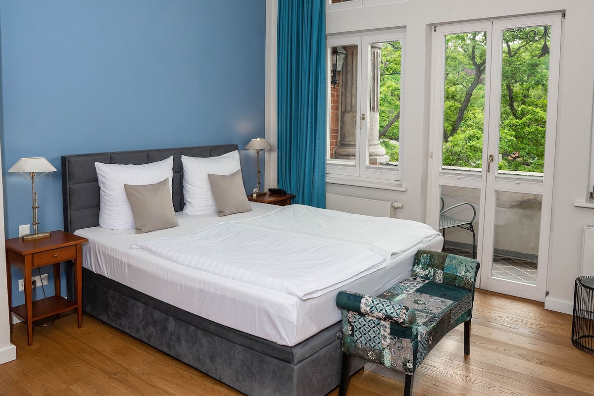 Une chambre à coucher comprenant un lit, des tables de chevet, un banc et une fenêtre donnant sur un paysage verdoyant.