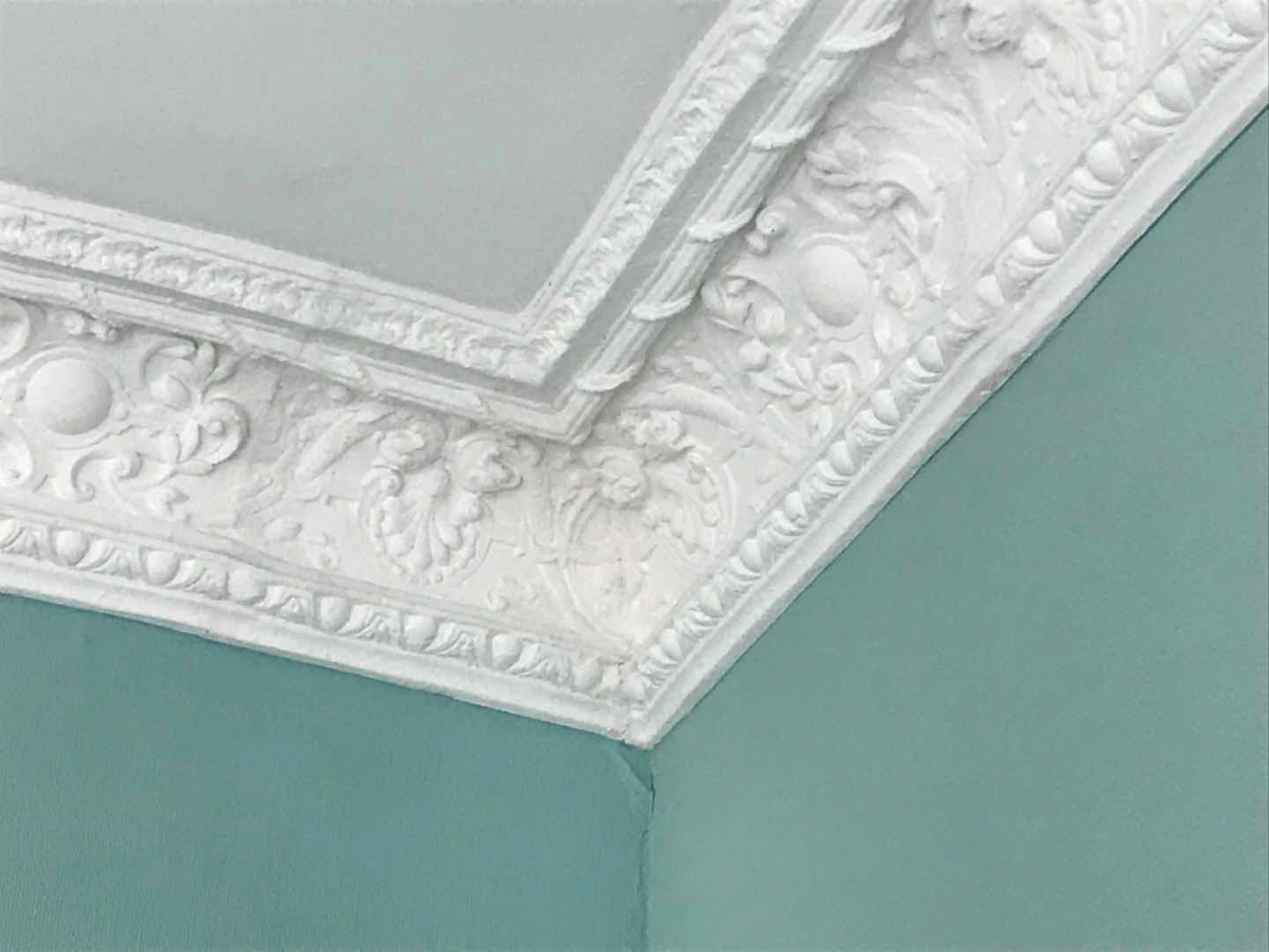 A white decorative molding with intricate designs on a teal wall.