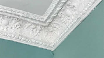 Eine weiße, dekorative Leiste mit filigranen Verzierungen an einer türkisblauen Wand.