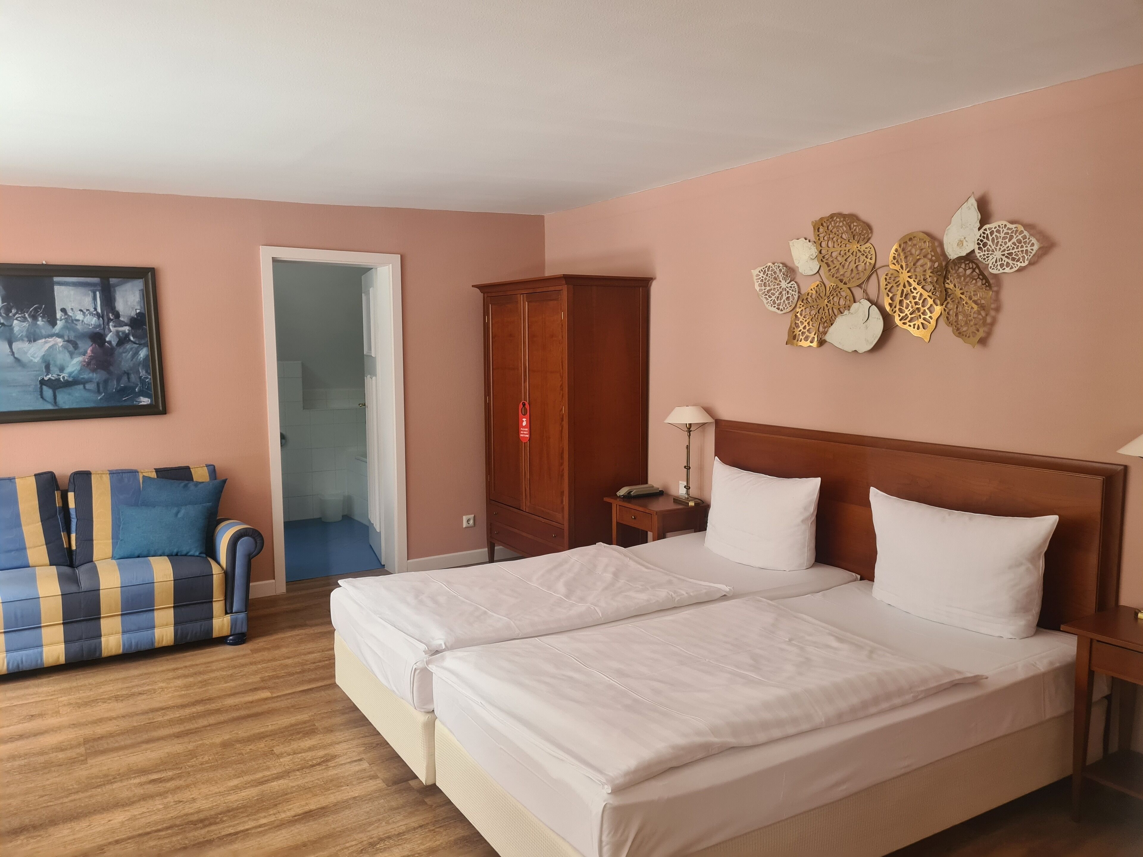 Ein Hotelzimmer mit Doppelbett, einer Schlafcouch mit gestreiften Kissen, einem Holzschrank, einem Gemälde an der Wand und Wanddekoration.