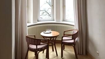 Ein Zimmer mit Erkerfenster, zwei Korbsesseln, einem kleinen runden Tisch und einer Heizung.