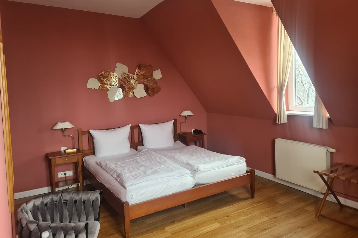 Une chambre avec un plafond en pente, un lit avec une literie blanche, une table de chevet en bois, une lampe et un radiateur.