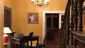 A hallway with a black and white checkered floor, a chandelier, a desk with a laptop, and a painting on the wall.