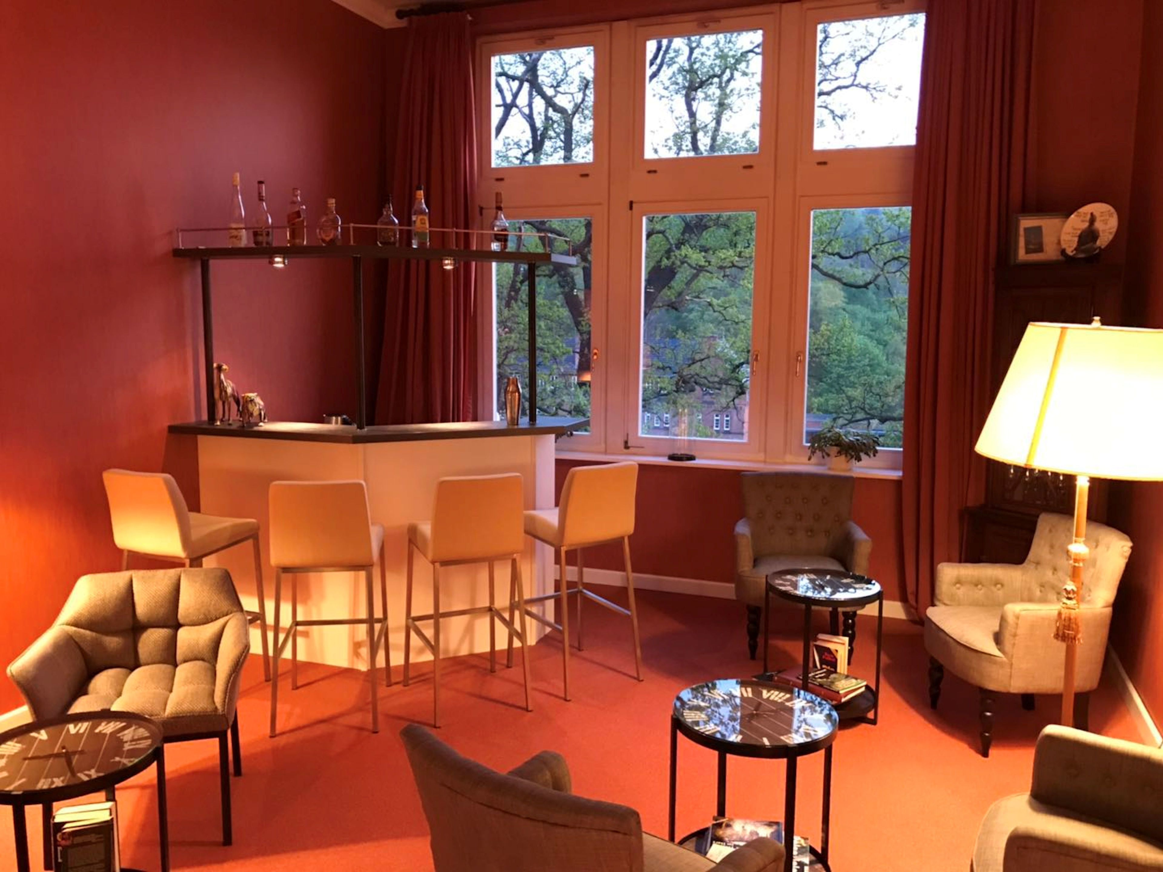A cozy room with a bar area, multiple seating options, and large windows offering a view of trees.