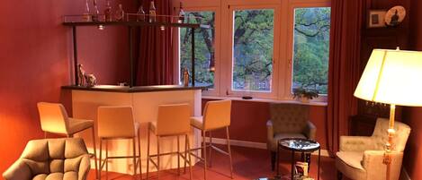 A cozy room with a bar area, multiple seating options, and large windows offering a view of trees.