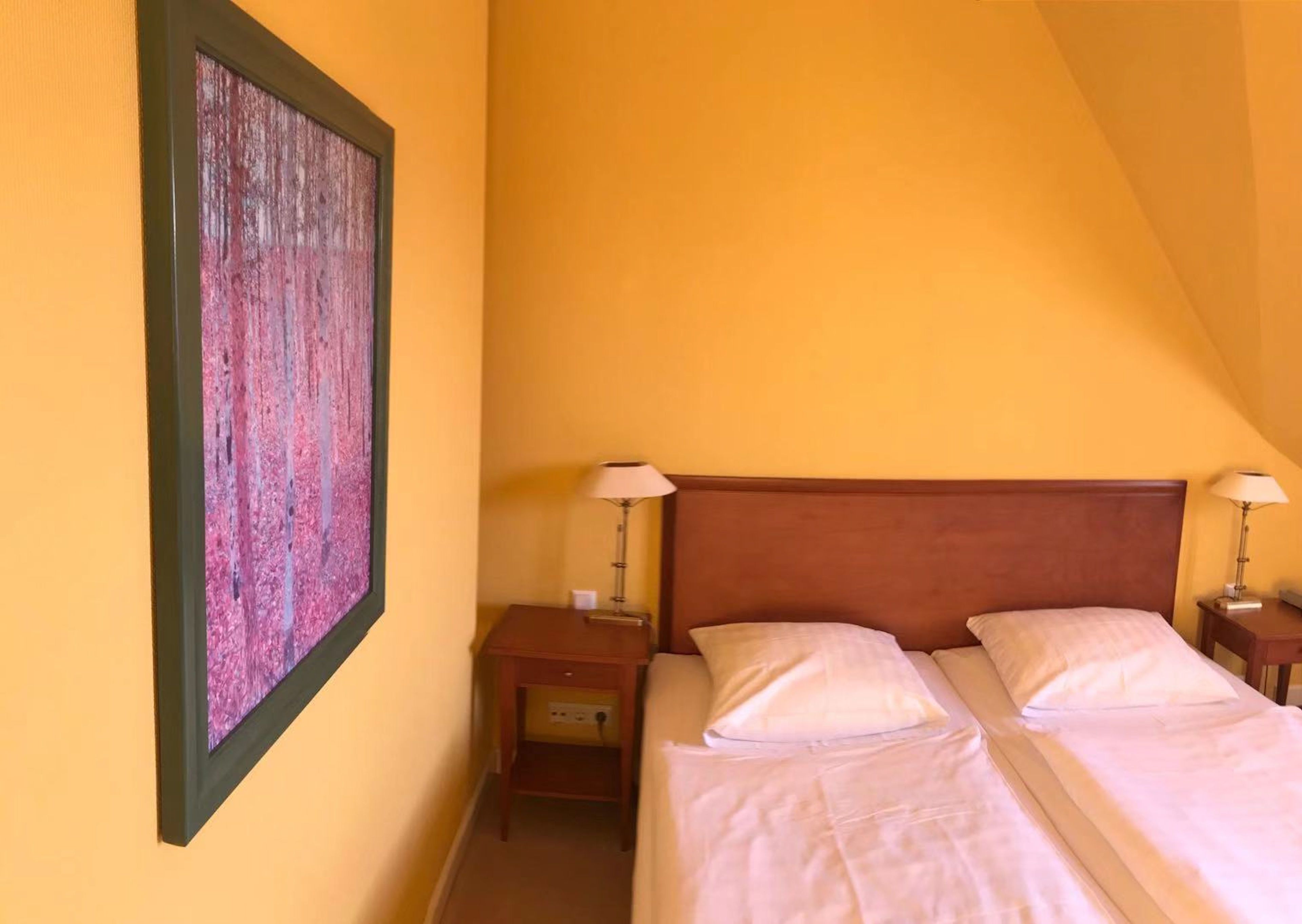 A room with a bed, two bedside tables, and a painting on the wall.