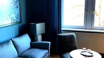 A room with a blue sofa, a small round table with a tray, a lamp, and a window with curtains.