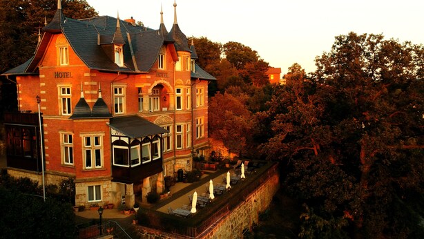 A historic hotel with a prominent tower, a covered veranda, and a stone wall surrounding the property. - Hotel Villa Viktoria Luise (Blankenburg)