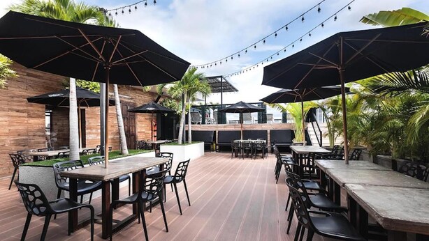 An outdoor patio with wooden tables and chairs, black umbrellas, and string lights. - Hotel Cartagena DC (Cartagena)