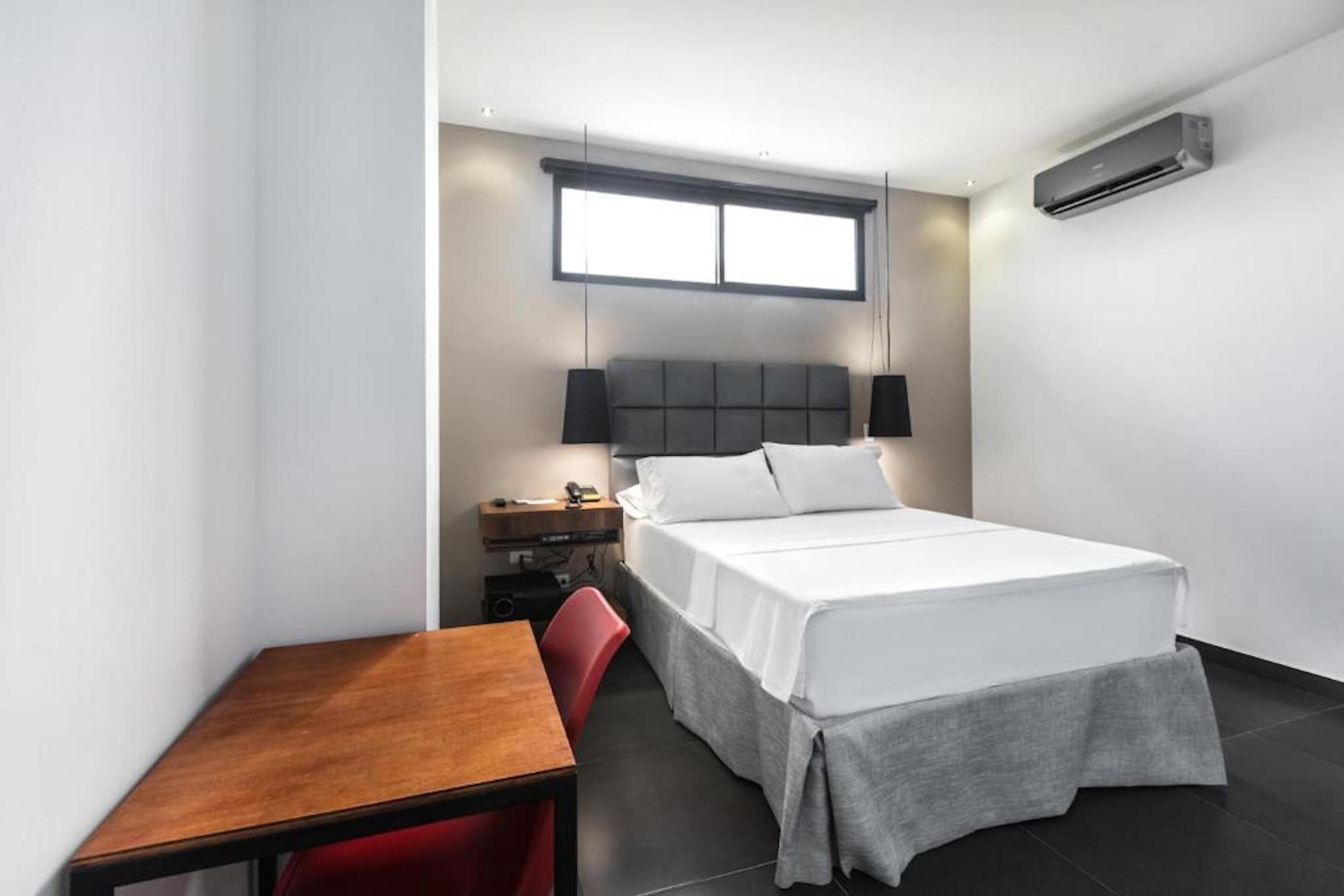 A modern hotel room with a bed, bedside table, chair, and a desk.