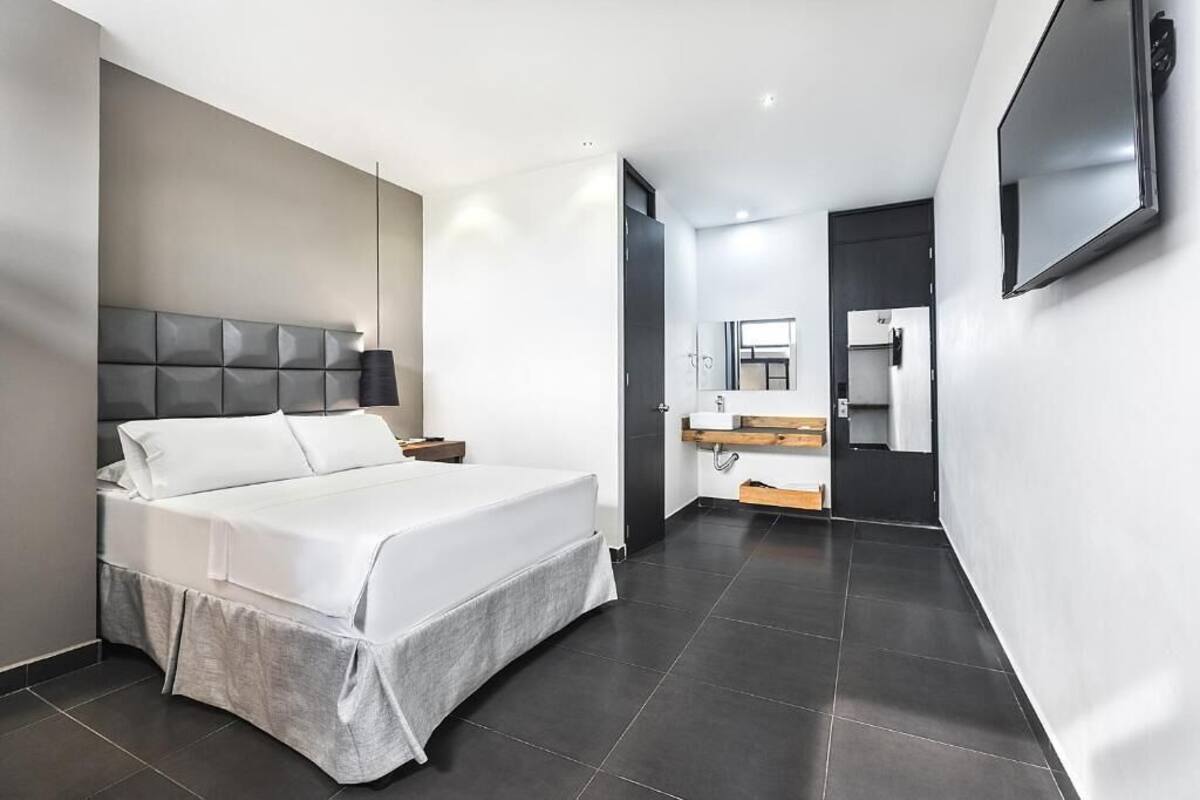 A modern hotel room with a large bed, a flat-screen TV, a bathroom with a sink and mirror, and a door leading to another room.