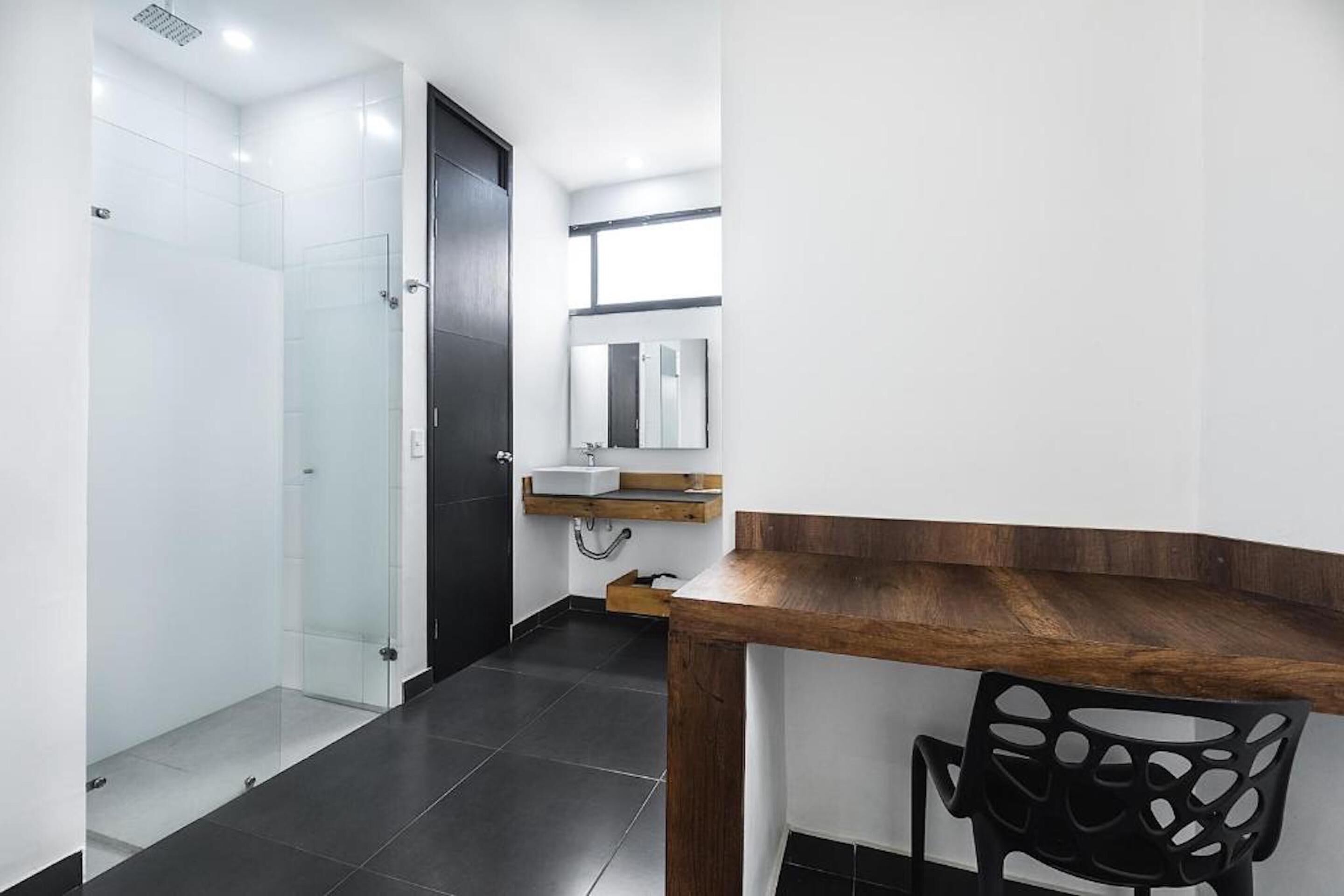 Een moderne badkamer met een glazen douchecabine, een houten wastafelmeubel met een wastafel en een zwarte stoel.